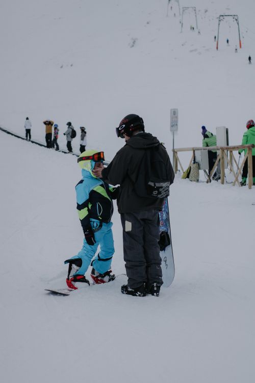 Free A man and child in winter gear preparing to snowboard on a snowy slope. Stock Photo