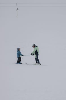 A father teaches his child skiing on a snowy slope during winter.