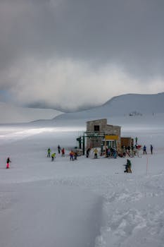 A group of skiers gather at a snow-covered mountain resort under overcast skies