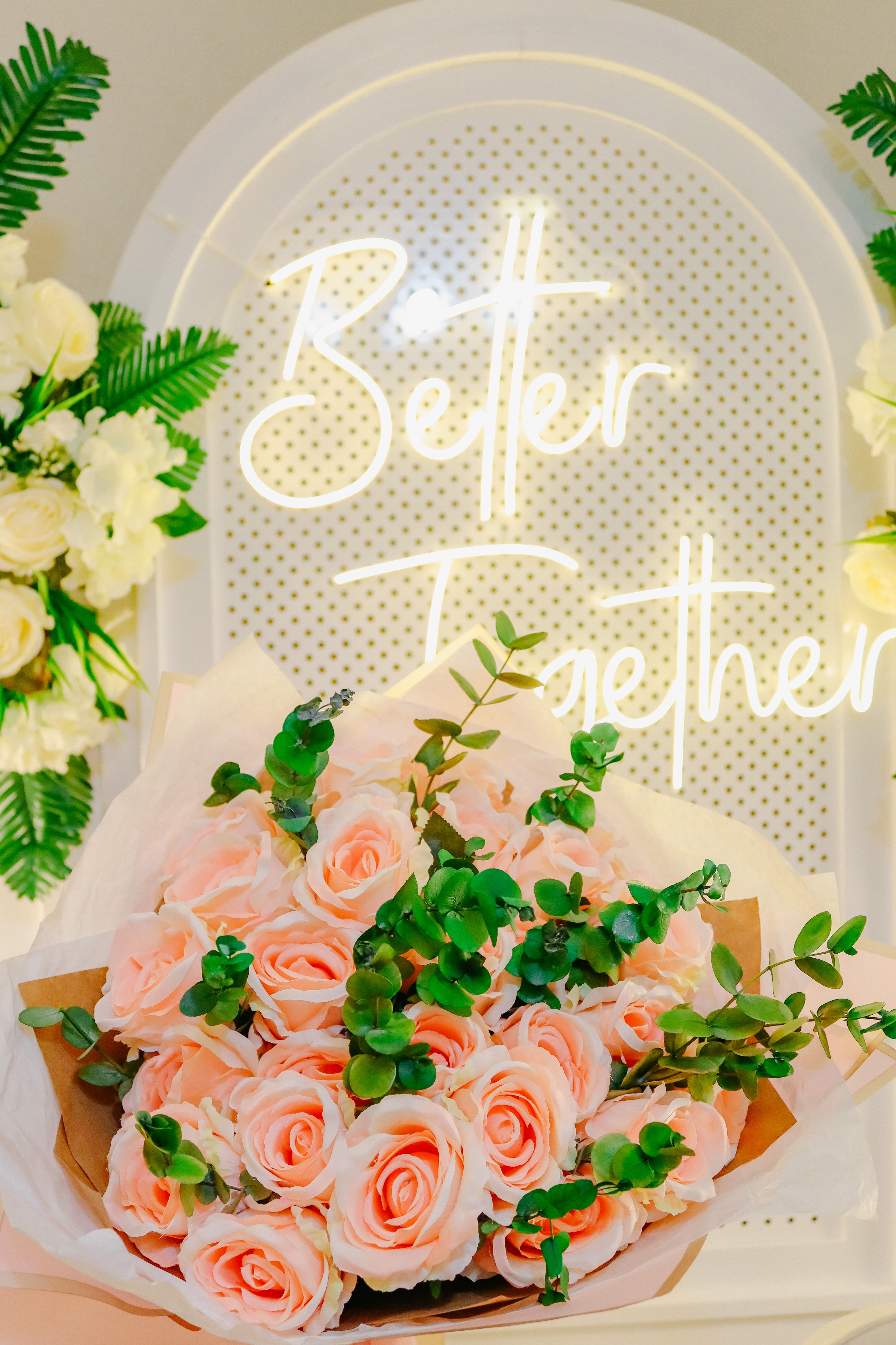Charming bouquet of pink roses with greenery in front of 'Better Together' neon sign.