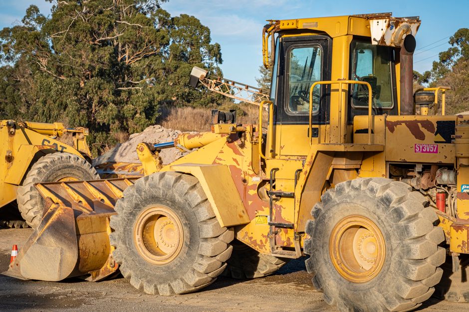Yellow excavator with large tires at a construction site surrounded by trees under daylight.