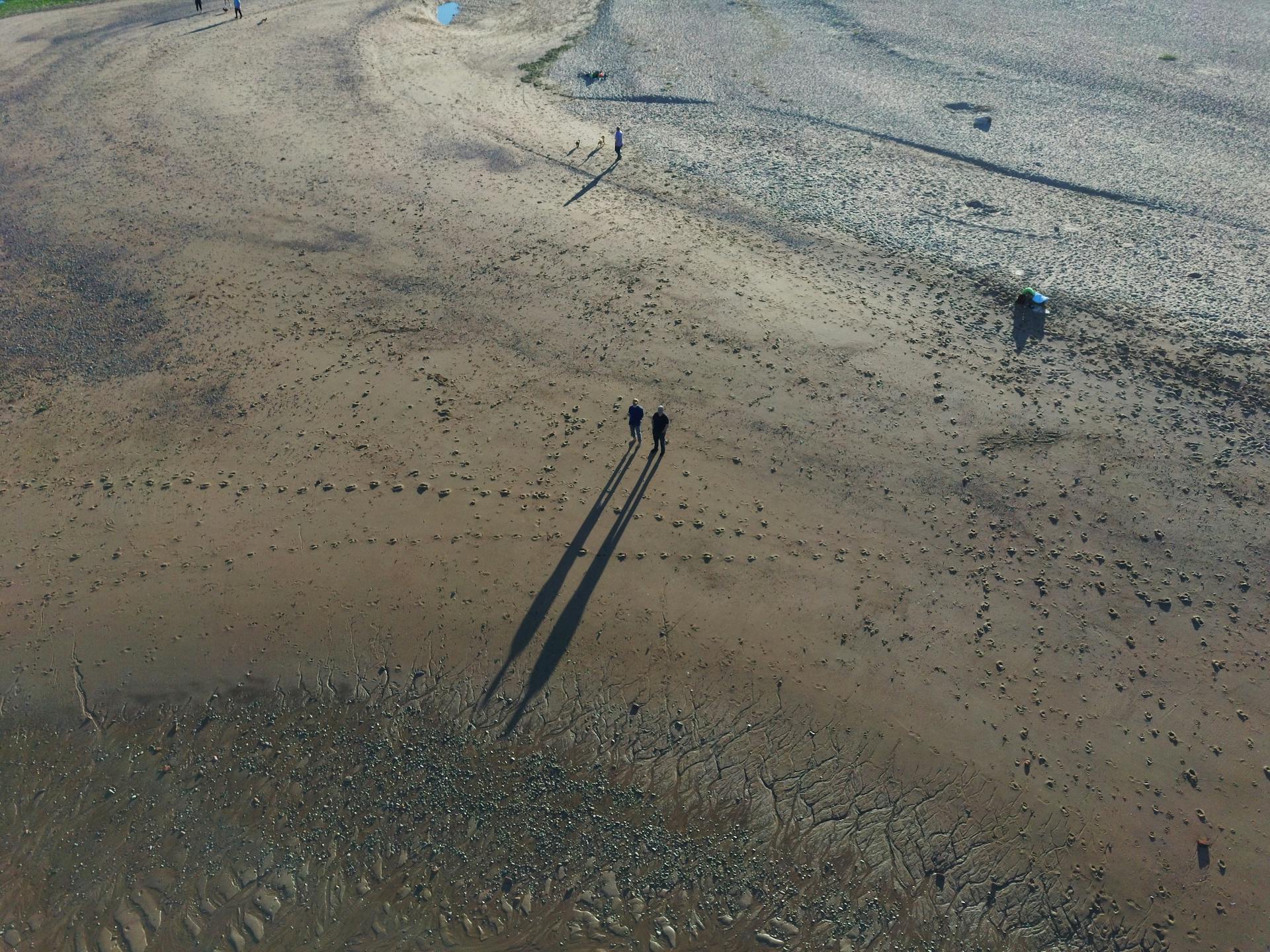 Aerial drone shot of people walking on Bridge of Don beach in Scotland, showing shadows and sandy landscape.