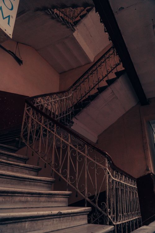 Free An atmospheric view of an indoor staircase featuring ornate iron handrails and dim lighting. Stock Photo