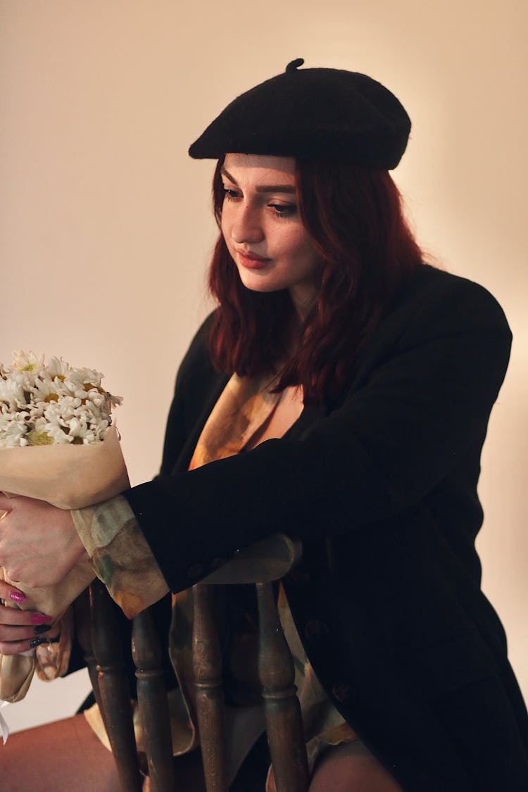 Woman In Beret Sitting On Chair With Flowers In Studio