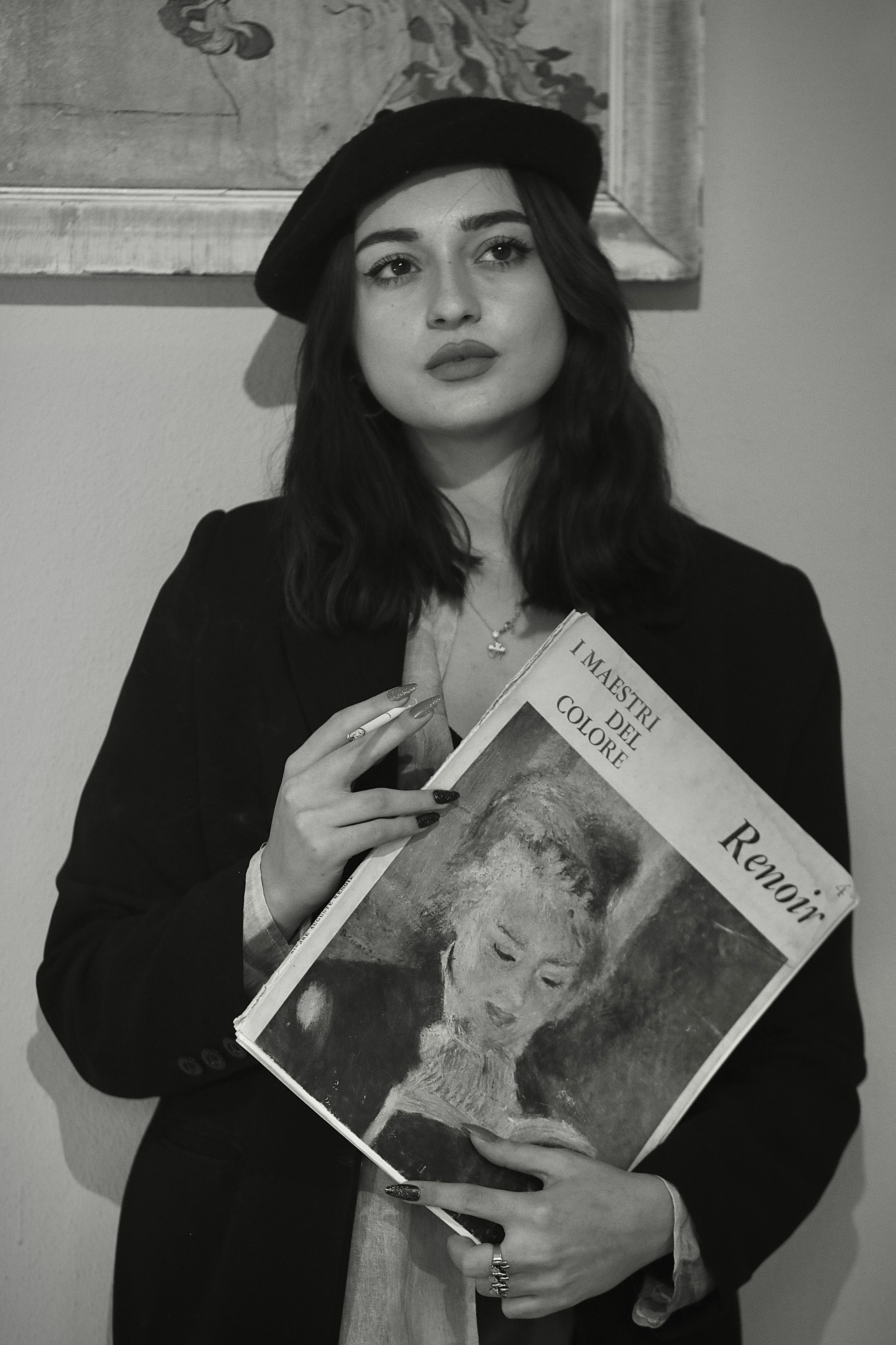 Black and white portrait of a woman holding a Renoir-themed book, showcasing classic style and elegance.