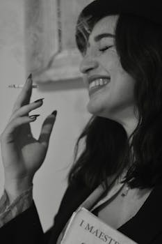 Black and white portrait of a laughing woman holding a cigarette, exuding charm and mystery.