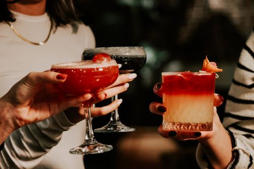 Free Three women clink colorful cocktails in a festive indoor bar setting. Stock Photo