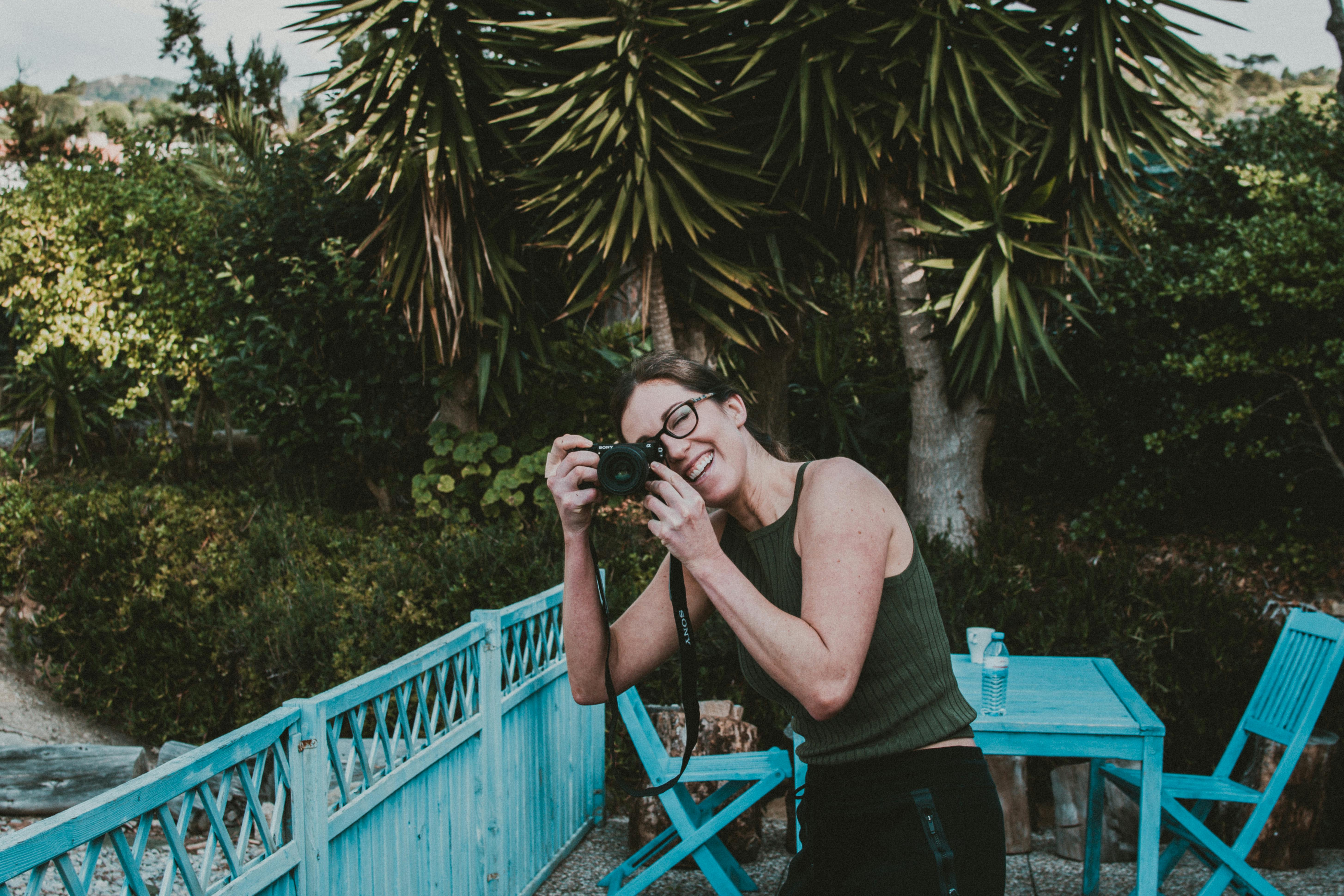 Woman enjoying outdoor photography with a camera against a lush green backdrop.