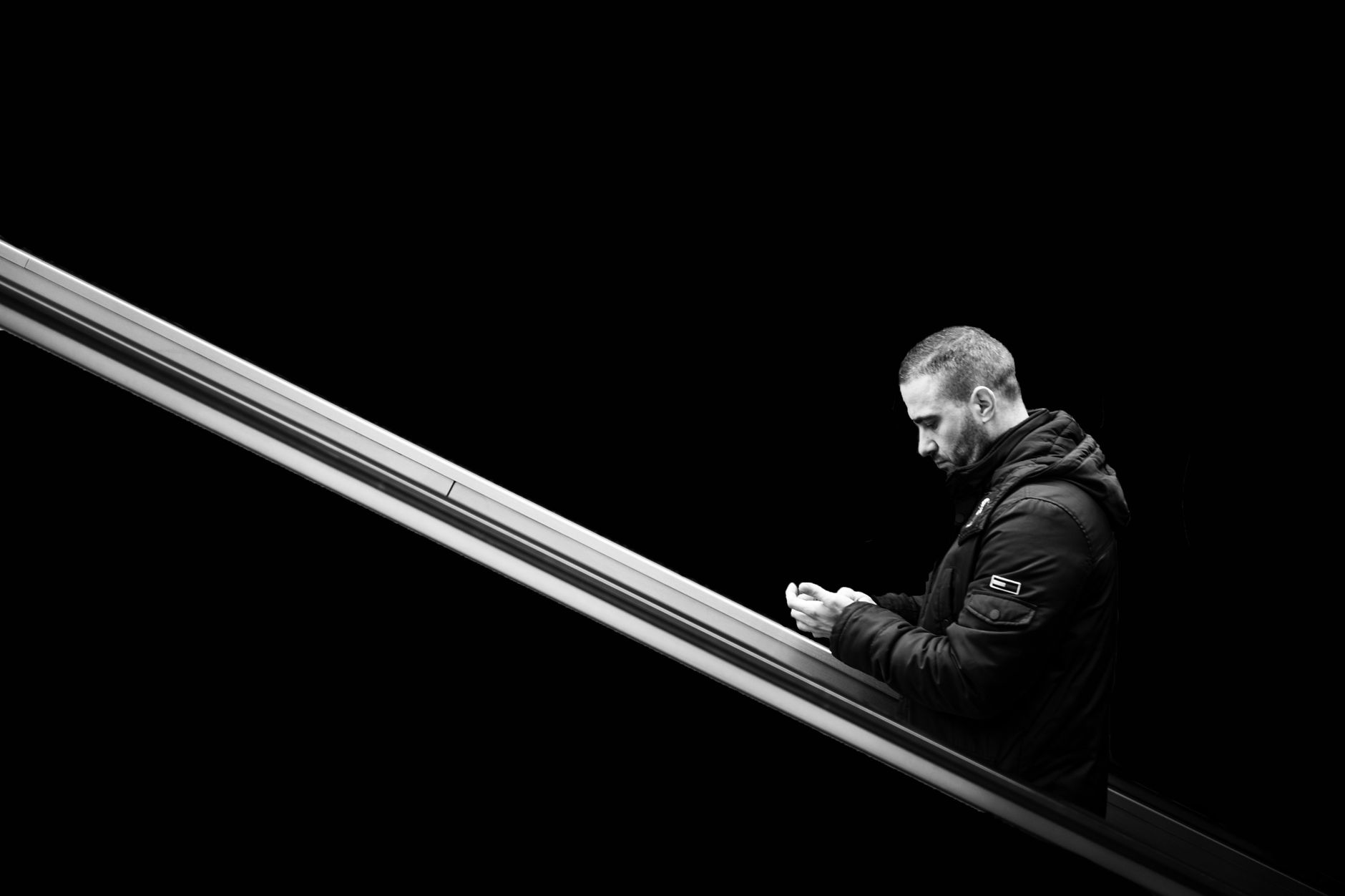 Black and white portrait of an adult man on an escalator using his phone.