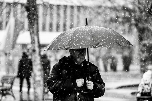 Free A monochrome image of a man sheltering under an umbrella during a snowstorm. Stock Photo