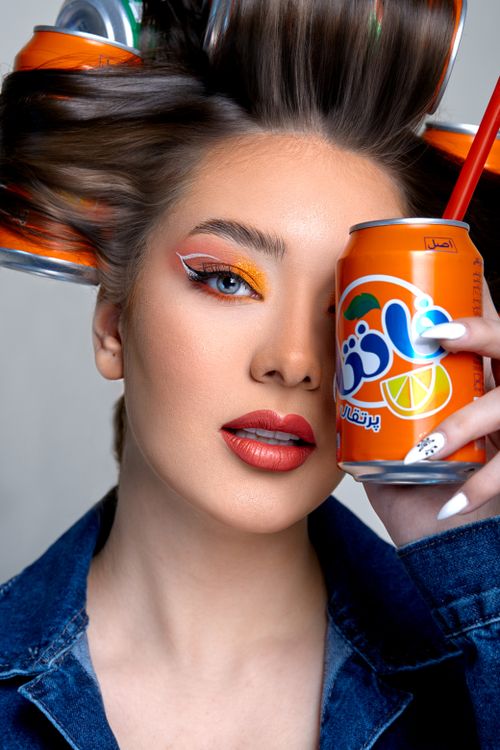 Free Fashionable woman holding a vibrant can of orange soda with striking makeup. Stock Photo