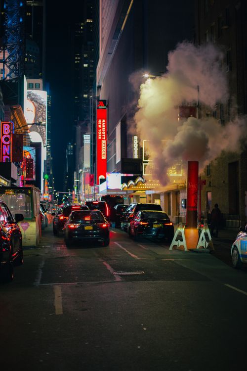 Free Nighttime downtown city street with cars, vapor, and vibrant billboards creating a lively urban ambiance. Stock Photo