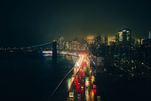A dramatic view of a city at night with illuminated buildings and bridge under mist.