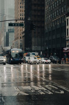 Street view of Manhattan with traffic on a rainy day, showcasing urban life and architecture.