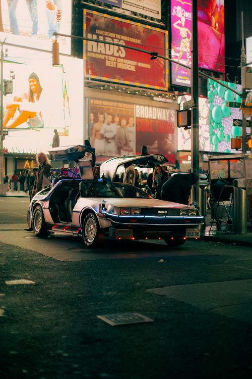 Free A vintage Delorean car with open doors parked in bustling Times Square at night with bright billboards. Stock Photo