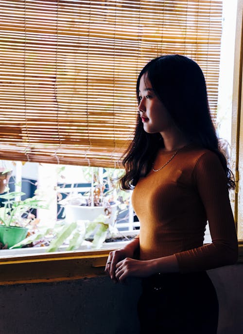 Woman Standing Beside Window Blinds and Plants