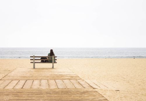 Free A lone figure sits on a bench overlooking the serene sea at a Los Angeles beach. Stock Photo