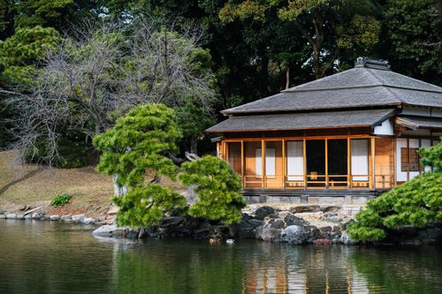 Free Tranquil Japanese house with a thatched roof by a serene pond in Tokyo park. Stock Photo