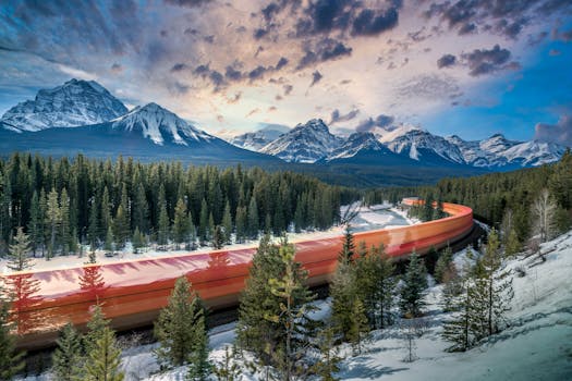 A red train speeds through a snowy forest with majestic mountains in the background.