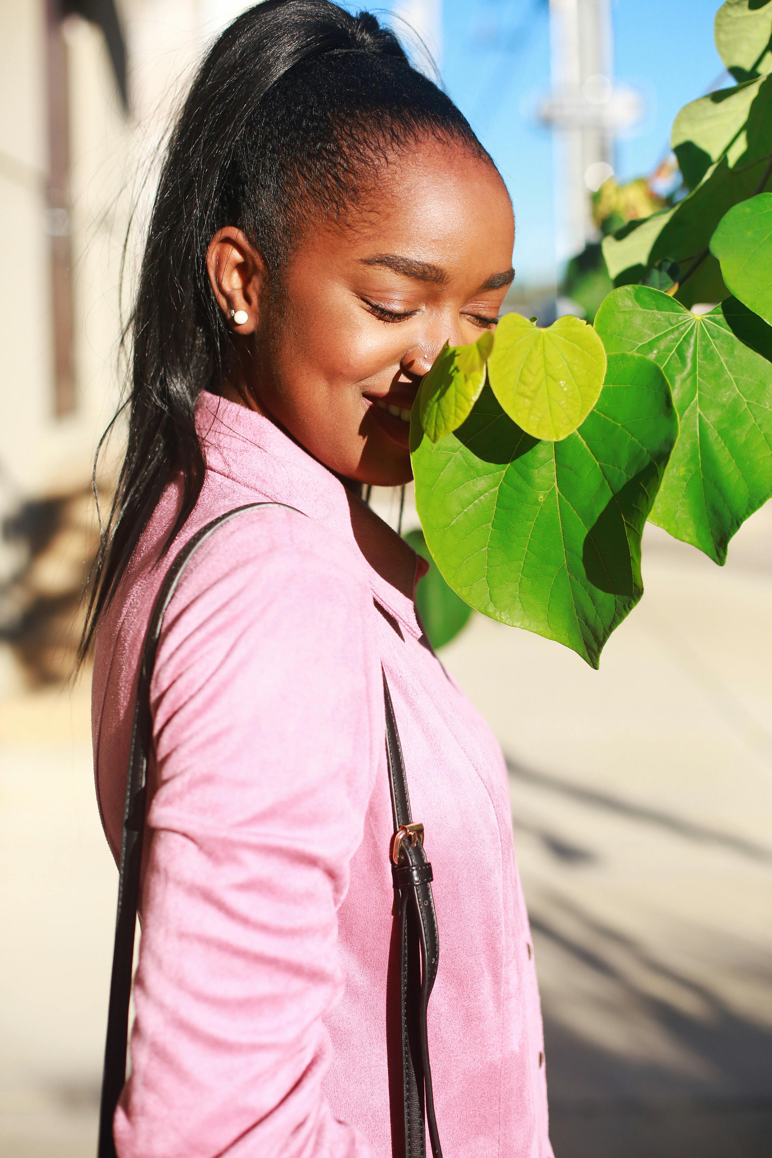 一位身着粉衣、气质别致的黑人女子，正在明媚的阳光下于户外摆着姿势