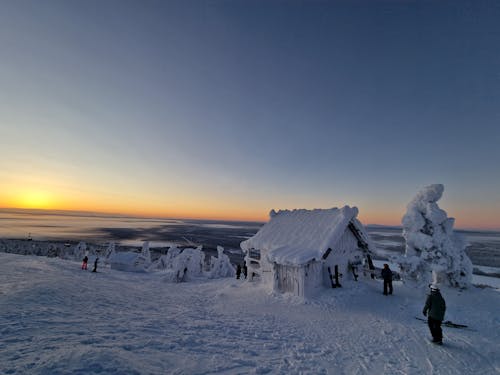 People near Wooden House in Snow at Sunset
