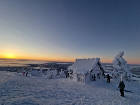 Serene winter scene with snowy cabin at sunset, surrounded by deep snow and distant horizon.