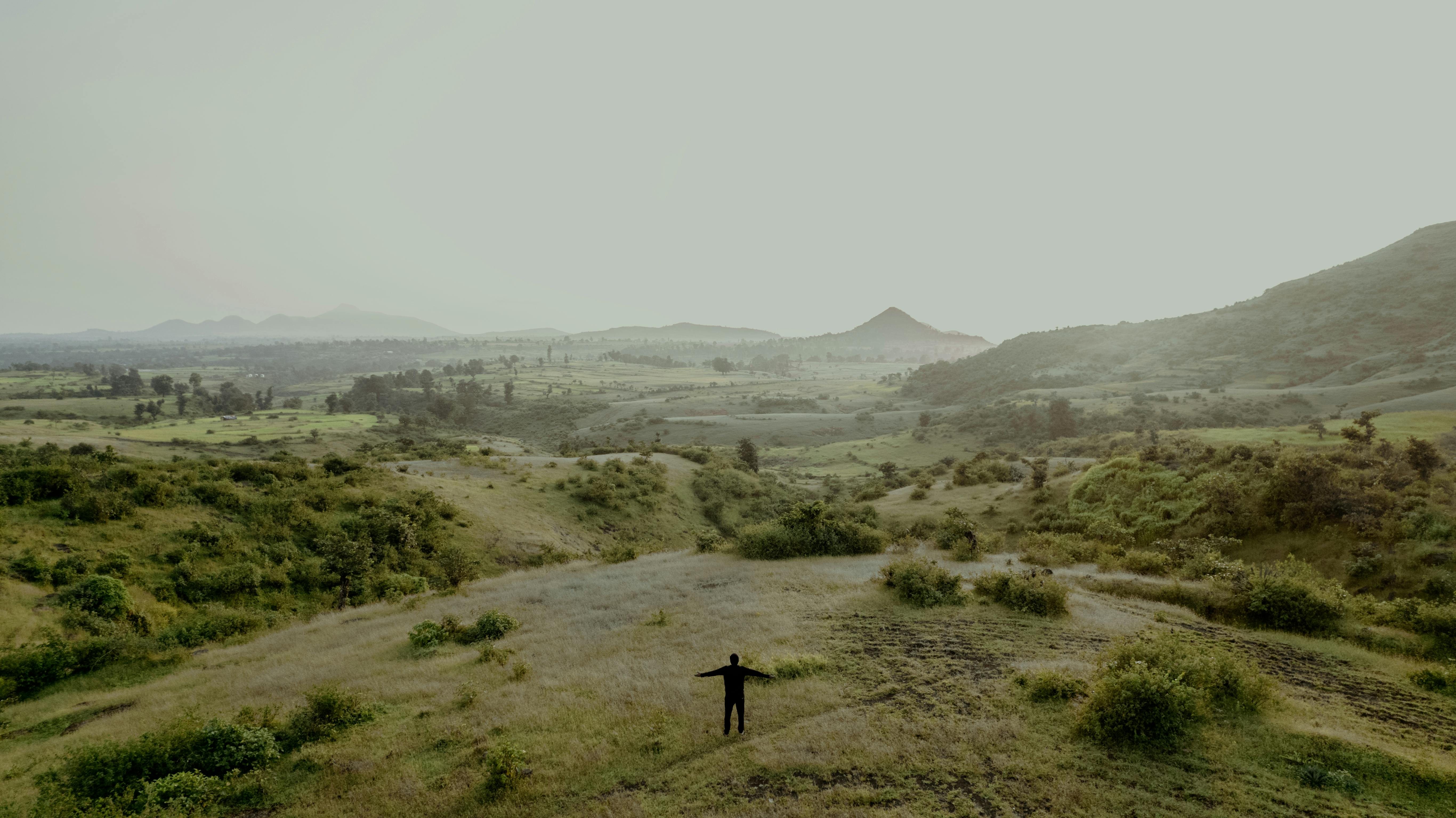 Serene landscape in Surat, India, with misty hills and a lone silhouette.