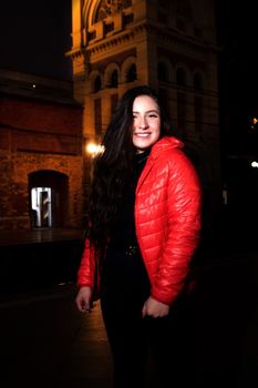 Smiling woman in red jacket standing outdoors at night in São Paulo, Brazil.