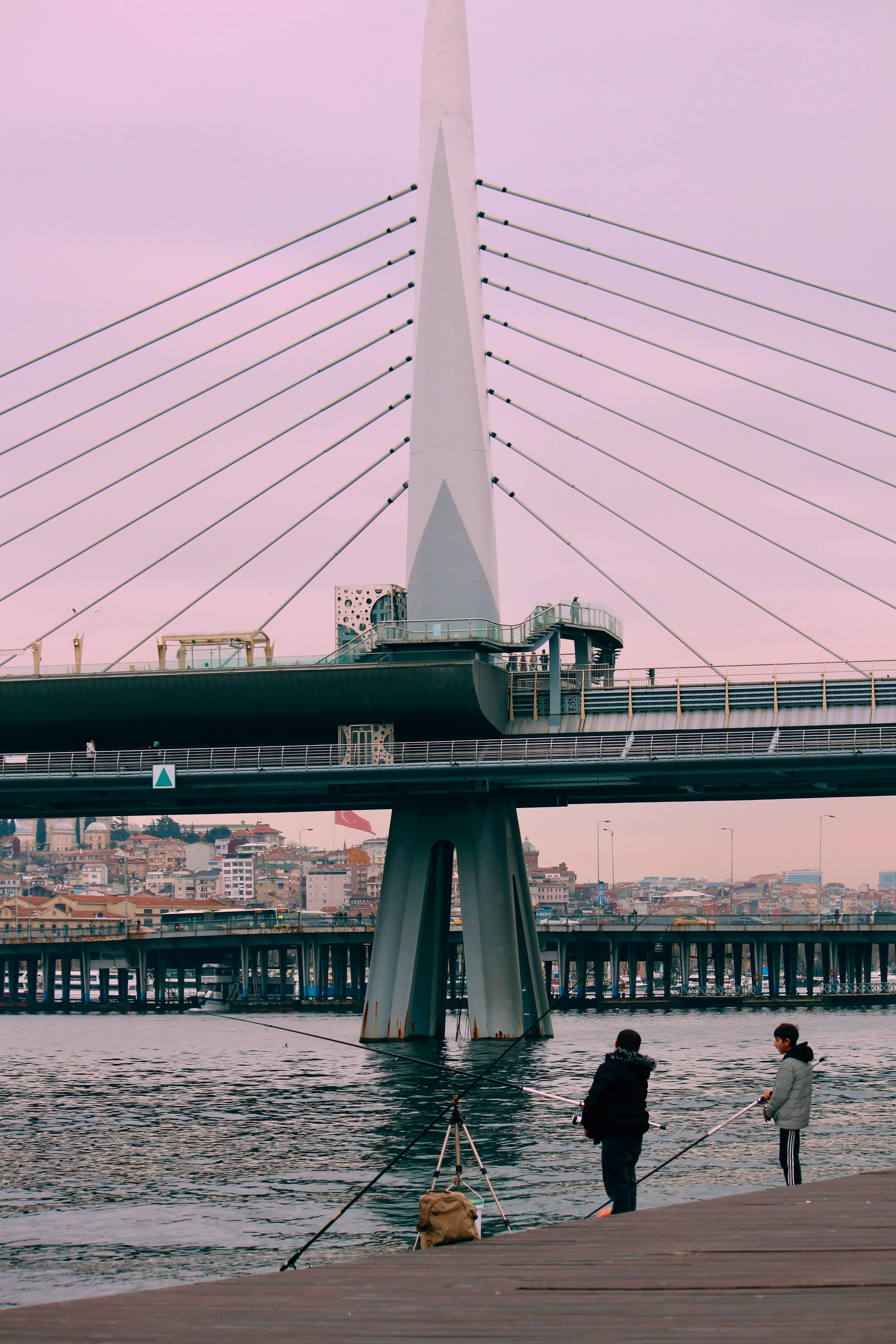 Fishermen casting lines by an iconic Istanbul bridge during an overcast dusk.