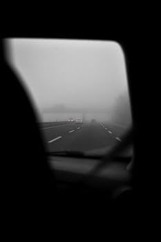 Black and white image of a foggy highway seen from a car window, creating a moody and mysterious vibe.