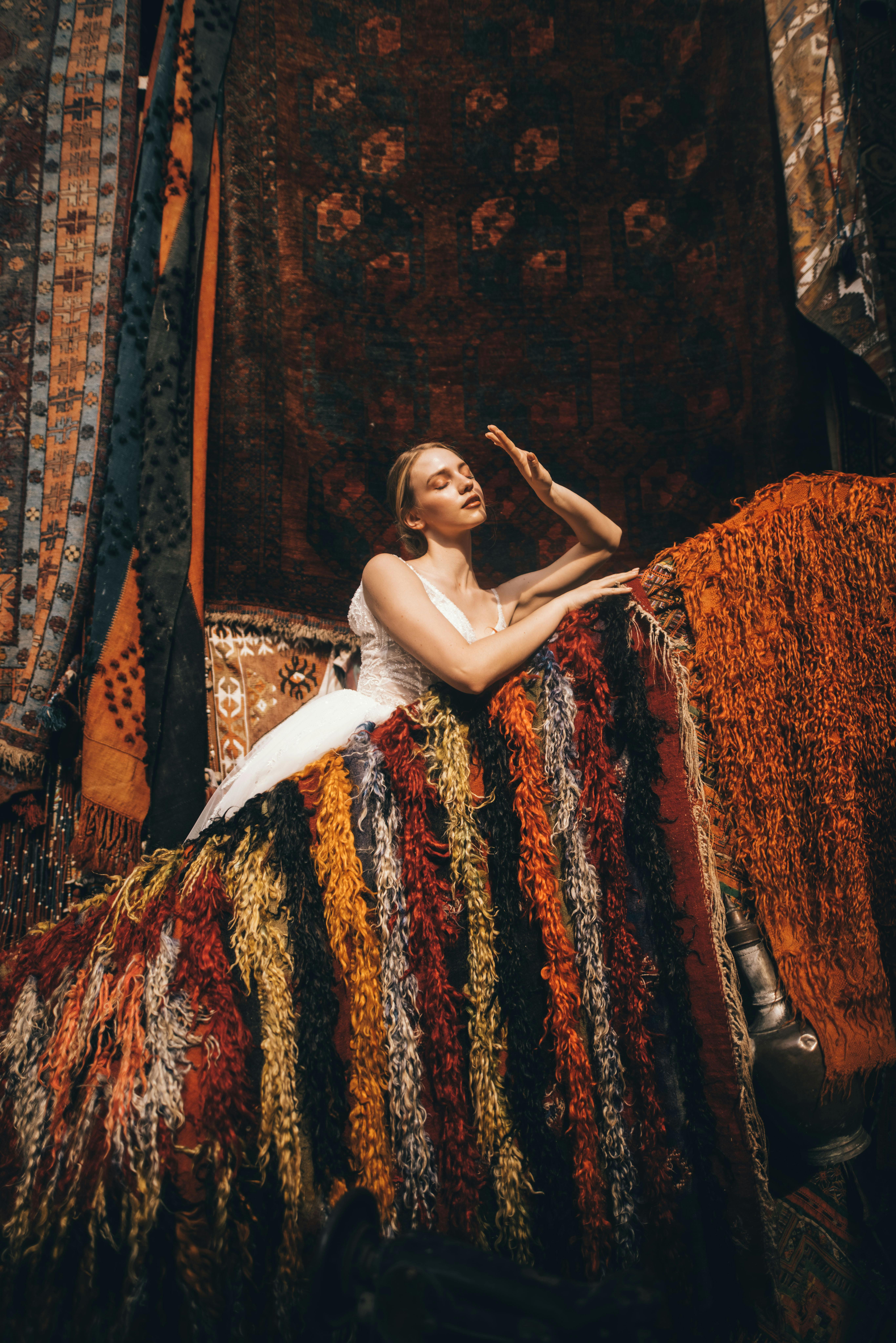 Blonde woman posing gracefully with vibrant textiles in a rich fabric setting.