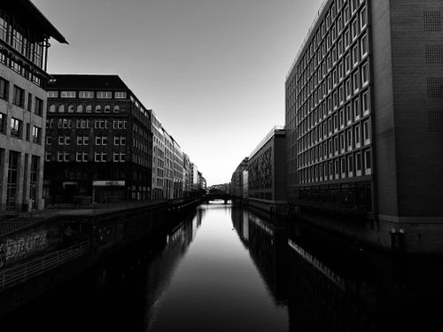 Free Monochrome urban scene featuring a canal flanked by geometric building facades. Stock Photo