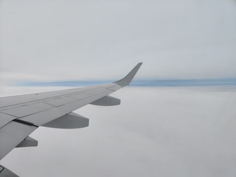 View of an airplane wing over a blanket of clouds during daylight flight.