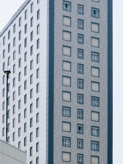 Free Close-up of a gray high-rise building with repetitive windows and a streetlight. Stock Photo