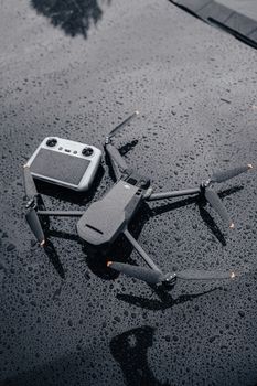 Close-up of a drone and controller on a wet surface, capturing rain details.