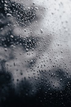 Close-up of raindrops on a glass window with a blurred natural background.