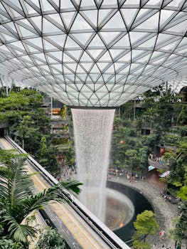 Explore the iconic Rain Vortex waterfall at Singapore's Jewel Changi Airport, a stunning indoor forest landmark.