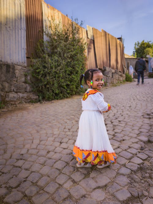 A Young Girl in White Dress Smiling while Standing on the Street