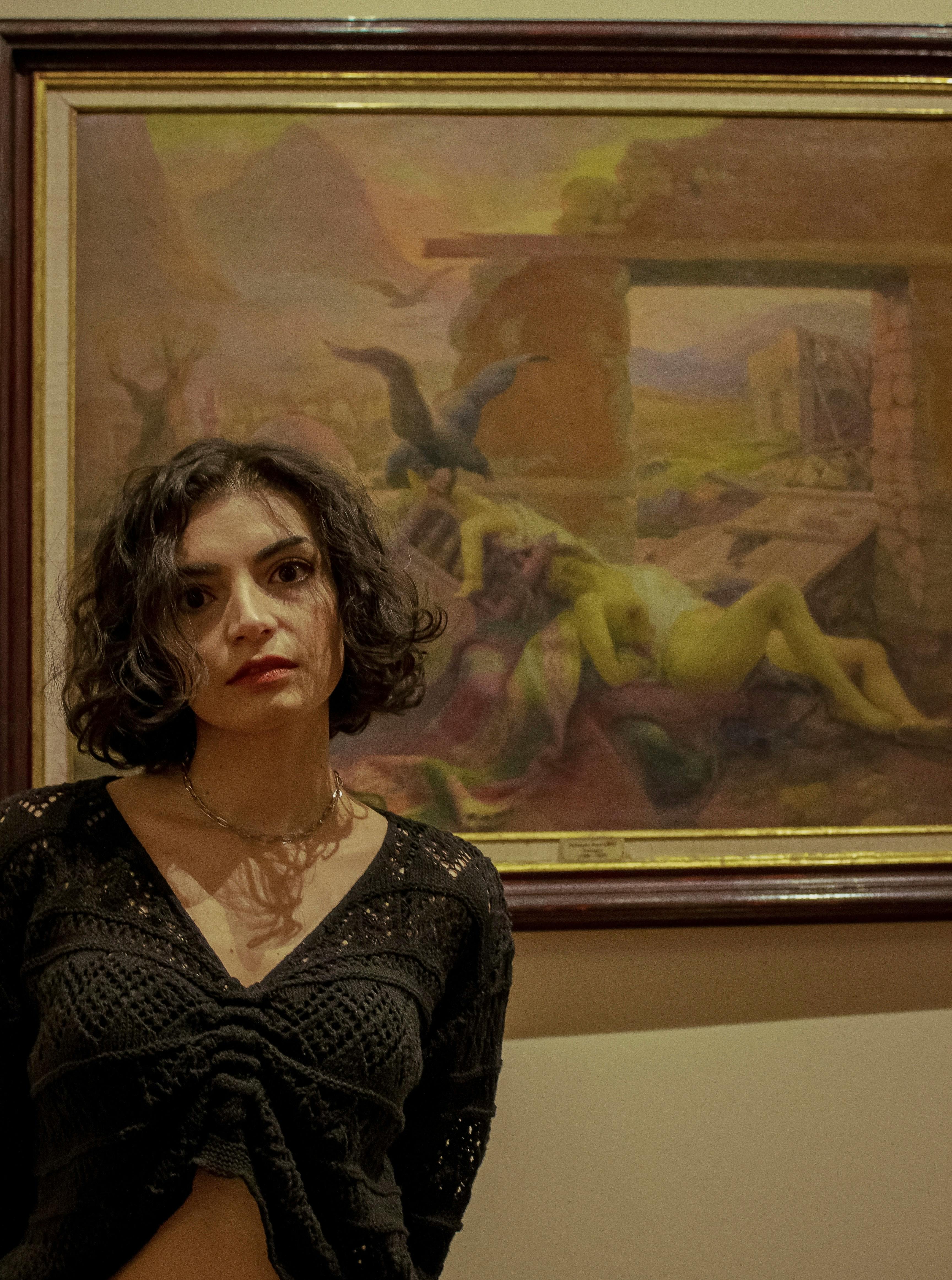 Free Portrait of a woman standing by a classic painting in a museum setting. Stock Photo