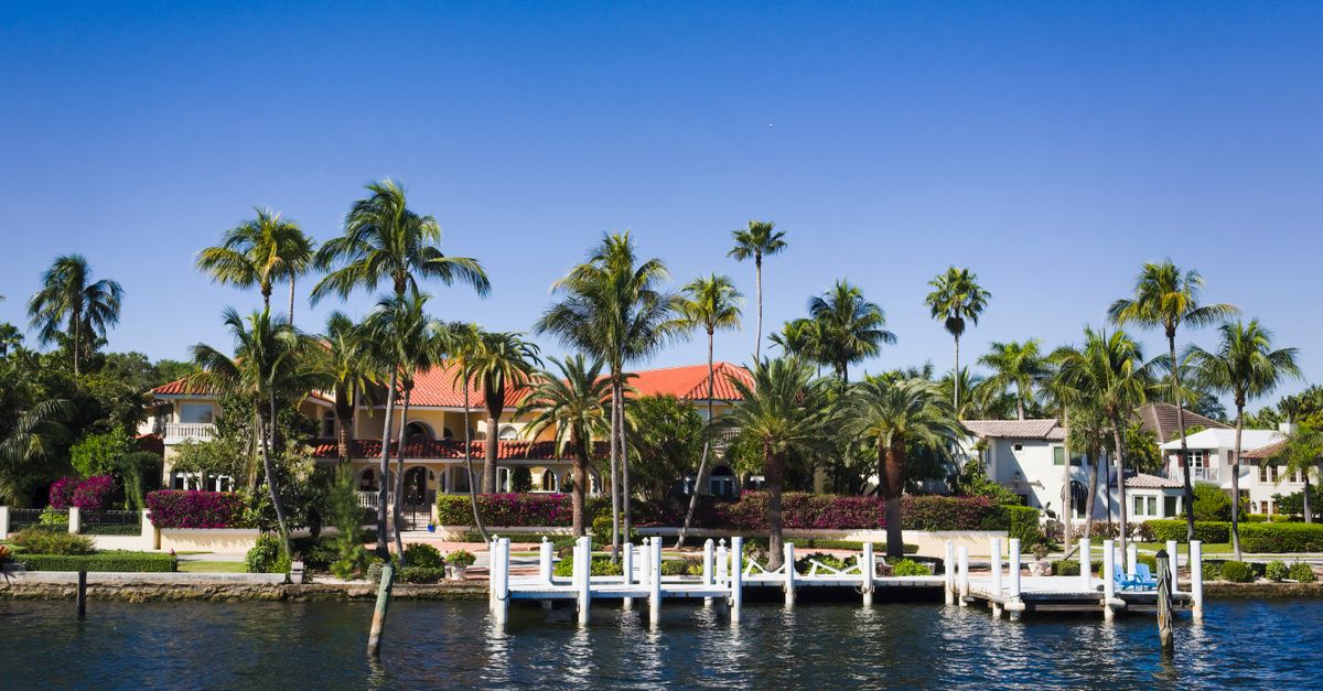 Scenic view of waterfront villas with palm trees and a pier under a clear blue sky.