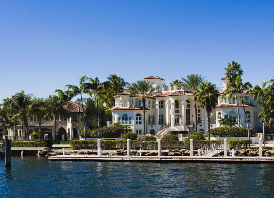 Elegant waterfront mansion with palm trees and clear blue sky showcasing opulence and coastal vibe.