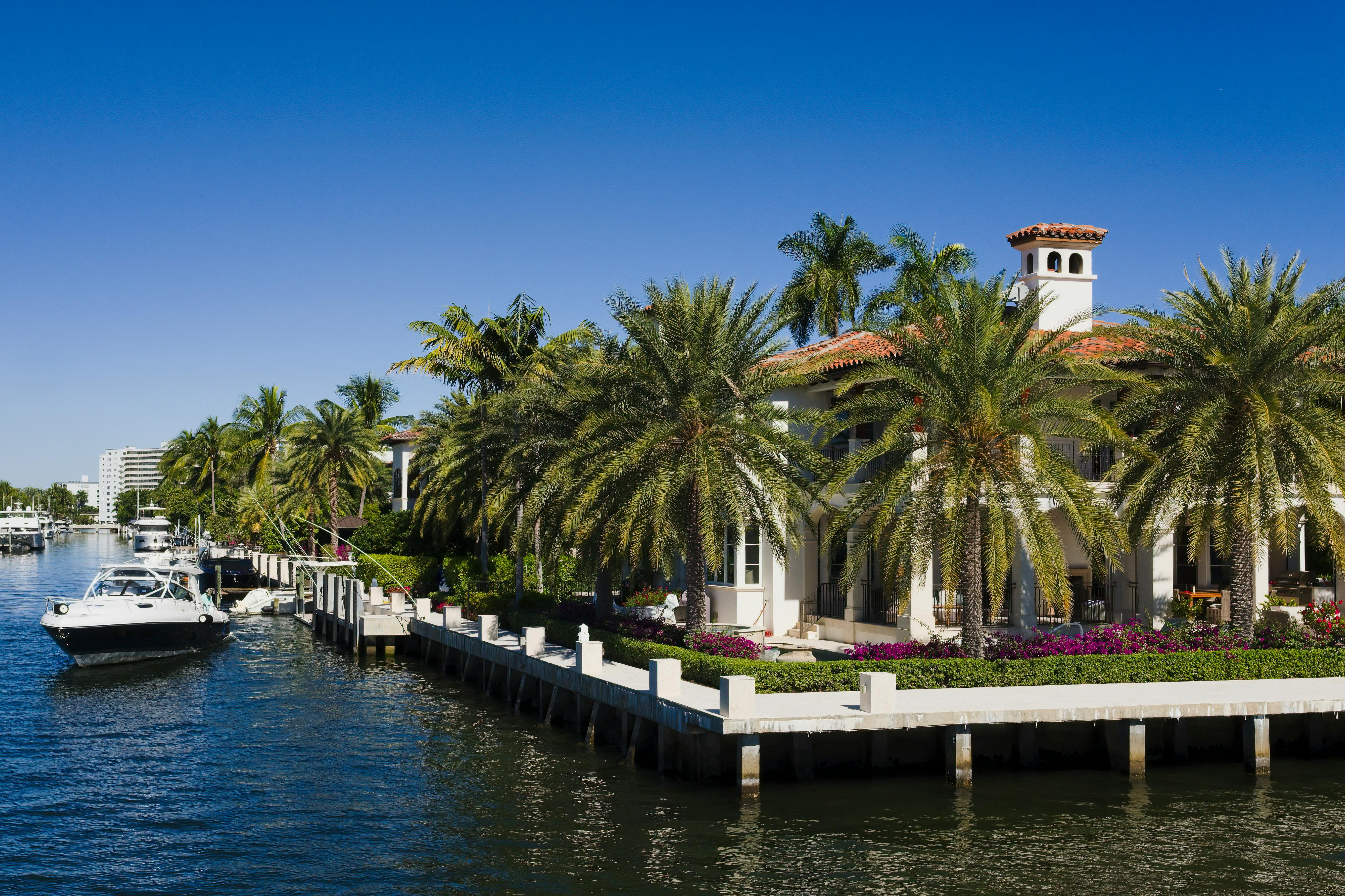 Elegant waterfront mansion with palm trees in Fort Lauderdale, Florida under a clear blue sky.
