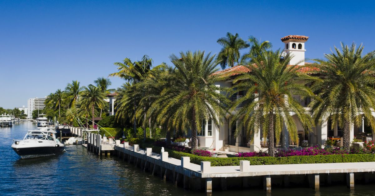 Elegant waterfront mansion with palm trees in Fort Lauderdale, Florida under a clear blue sky.