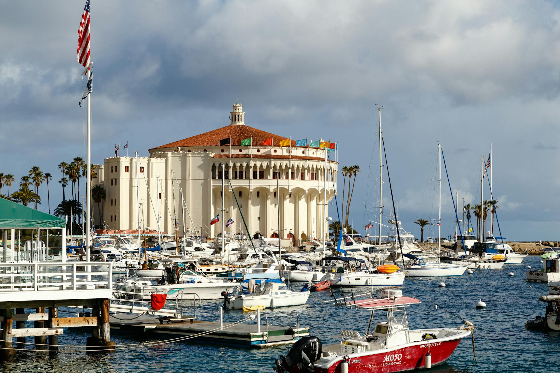 Scenic view of Avalon Harbor featuring the iconic Catalina Casino with boats docked and the American flag waving.