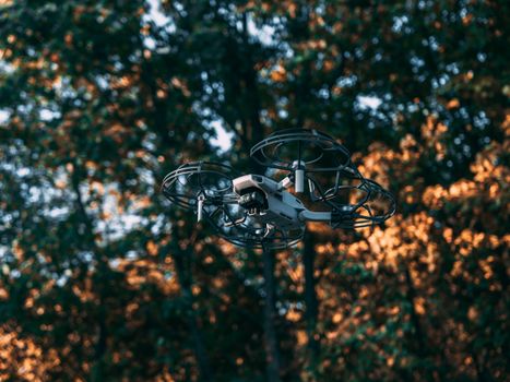 A drone hovering mid-air against a blurred autumn forest background.