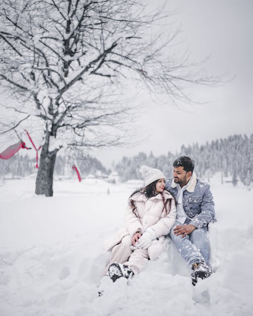 A Young Couple Sitting Outside in Snow and Smiling 