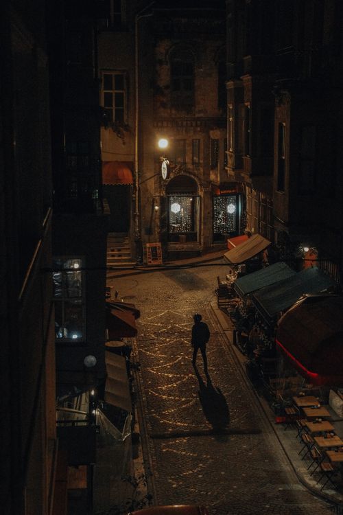 Free A solitary figure walks through a dimly lit street at night, casting shadows. Stock Photo