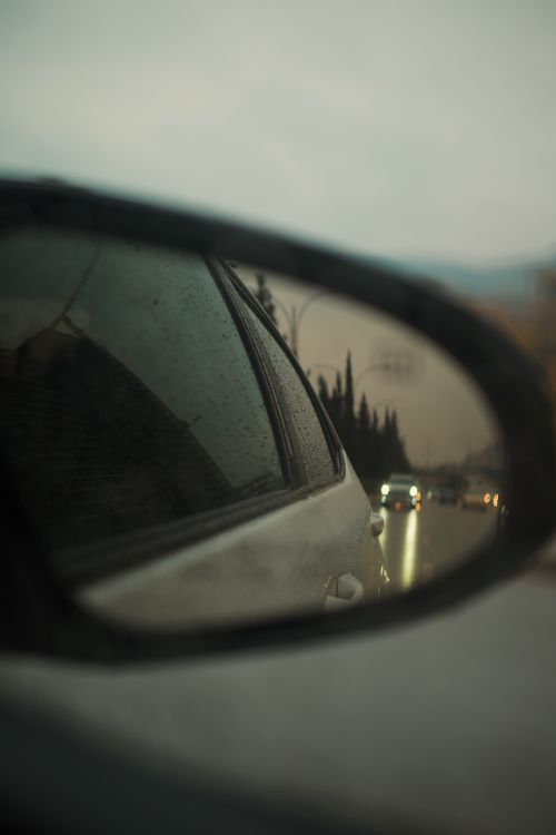 Free A serene view of moving traffic reflected in a car's side mirror on a cloudy day. Stock Photo