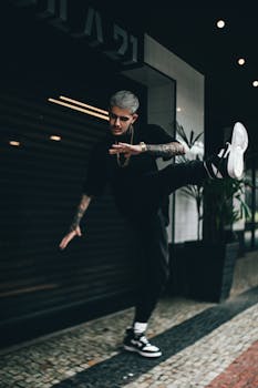 Dynamic urban shot of a tattooed man kicking in style, showcasing modern street fashion.
