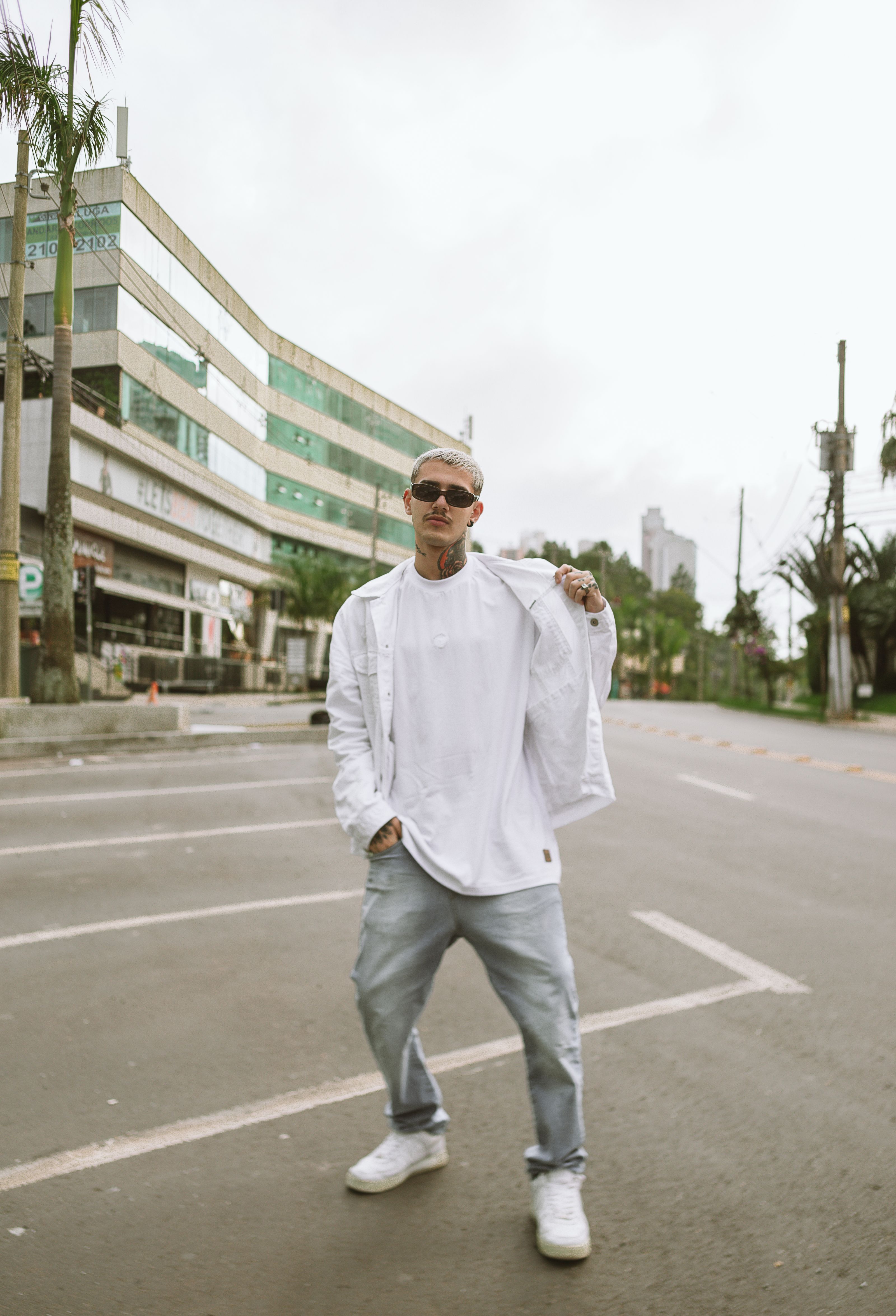Homem estiloso em um traje branco posando confiantemente em uma rua urbana.